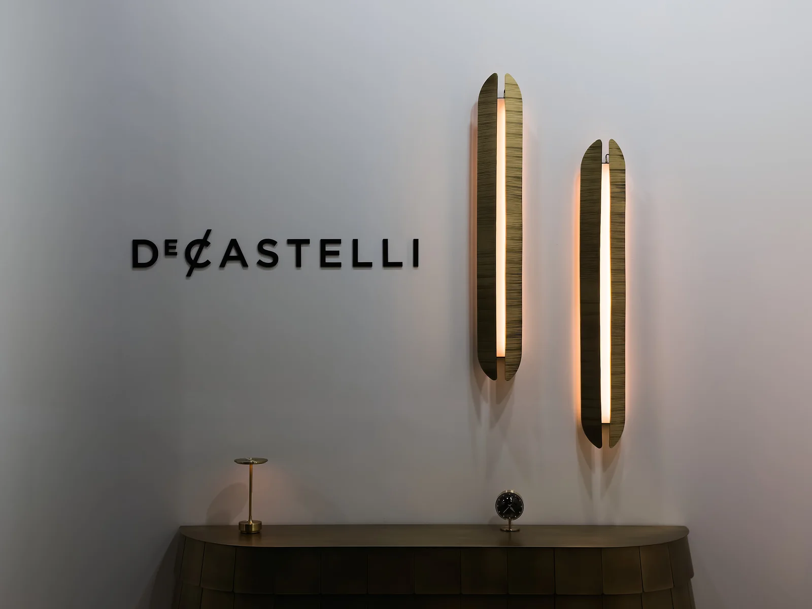 Логотип DE CASTELLI и вертикальные светильники на стене